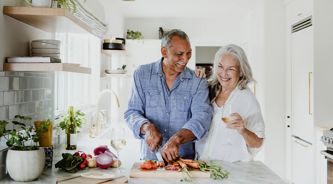 Mature man and woman in the kitchen smiling and cutting vegetables
